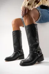 Botas de cuero negras con caña alta, taco cuadrado y detalle de arnés con hebillas metálicas.