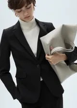 Blazer negro de diseño entallado, con solapas de muesca, hombros estructurados y cierre frontal de un solo botón. Presenta dos bolsillos de ribete delanteros y un bolsillo de ribete en el pecho.