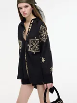 Camisa negra con bordados dorados, cuello camisero, botones frontales y bajo irregular.