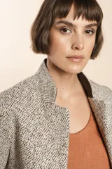 Chaqueta de sastrería color crudo con textura tweed, corte entallado, cuello mao y mangas largas.