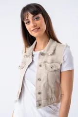 Chaleco beige de denim con cuello clásico, cierre frontal con botones metálicos, bolsillos delanteros con solapa y detalle de flecos en cuello, sisas y ruedo.