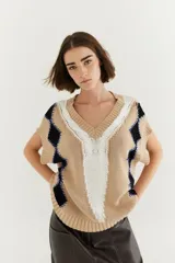 Chaleco de punto color beige con diseño de rombos negros y blancos, bordado a mano y detalles de lurex. Tiene cuello en V y sisas amplias.