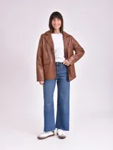 Blazer marrón de cuero sintético, con solapas de muesca, cierre frontal con dos botones y bolsillos laterales con solapa.