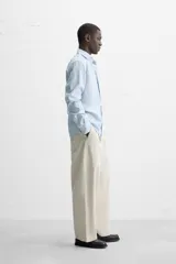 Camisa celeste a rayas verticales, de corte regular fit, con cuello italiano abierto, mangas largas con puños abotonados y cierre frontal con botones.