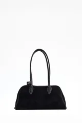 Cartera tipo bowling negra, confeccionada en material que simula gamuza o ante, con dos asas superiores de cuero liso negro. Presenta una forma alargada y redondeada en la base.