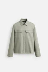 Sobrecamisa color arena de corte recto, con cuello solapa, cierre frontal con cremallera, manga larga con puños abotonados, dos bolsillos de plastrón con solapa en el pecho y dos bolsillos laterales en la costura de la cadera.