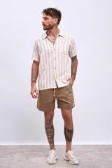 Camisa de manga corta color beige con rayas verticales marrones, cuello tipo cubano y bolsillo en el pecho.