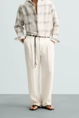 Pantalón color crema de lino, corte relaxed fit, con pliegues frontales, bolsillos laterales y traseros de vivo.