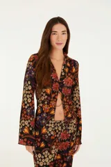 Camisa negra con estampado floral en tonos naranja, rojo y amarillo. Corte recto y fluido con cierre frontal con botones. Cuello clásico y manga larga.
