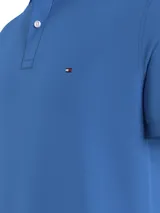 Chomba azul de Tommy Hilfiger, modelo 1985, de corte regular, con cuello tipo chomba, cartera de dos botones, logo bordado en el pecho y confeccionada en mezcla de algodón y poliéster.