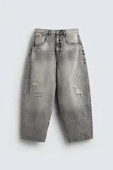 Pantalón de jean gris con lavado gastado, corte holgado, tiro medio, cinco bolsillos y roturas. Cierre frontal con cremallera y botón.
