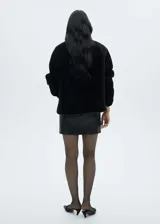 Chaqueta de pelo color beige con cuello alto, cierre frontal con botones y bolsillos delanteros.