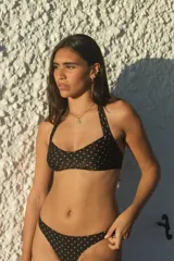 Conjunto de bikini negro con lunares color piel. El corpiño es tipo halter con tiras para atar en el cuello y la espalda. La bombacha es colaless.