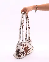 Cartera baguette de cuero con estampado animal print de vaca en tonos marrón y blanco. Tiene forro interior, un bolsillo amplio y broches laterales para ajustar el tamaño.