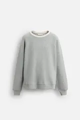 Sudadera gris de tejido compacto con mezcla de algodón y viscosa, corte relaxed fit, cuello redondo y mangas largas. El cuello y los puños tienen acabado en rib combinado a contraste en color crema.