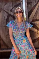 Vestido largo de poliéster con estampado floral en tonos celeste, amarillo y rosa. Diseño cruzado con escote en V y mangas cortas con volados.