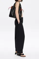 Bolso de mano negro con exterior de piel y estructura blanda. Incluye asa extraíble, bolsillo interior y etiqueta de tejido. Presenta logo metálico BIMBA Y LOLA con acabados metálicos plateados.