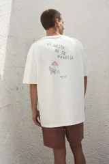 Remera blanca de algodón con estampado en la espalda con la frase "Follow the Waves" y dibujos de conchas marinas en color celeste.