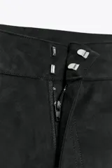 Shorts de tiro alto color negro con textura de gamuza, bolsillos delanteros y cierre frontal con cremallera y ganchos metálicos.