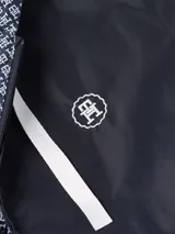 Cortavientos reversible con capucha y cierre de cremallera, con un lado liso azul marino y otro con estampado de monogramas TH en azul y blanco. Cuenta con bolsillos laterales y cordón ajustable en la capucha.