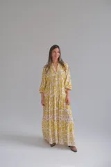 Vestido largo amarillo con estampado floral blanco, cuello en V, mangas 3/4 y corte escalonado.