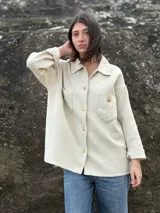 Camisa color crema tejida en lana, con cuello clásico, cierre frontal con botones dorados, dos bolsillos con solapa en el pecho y mangas largas con puños abotonados.