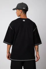 Remera negra oversize con mangas cortas y costuras a la vista en color blanco.