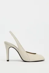 Zapato de tacón en piel color beige con abertura lateral, punta fina y cierre con tira ajustable. Tacón alto fino de 10,5 cm.
