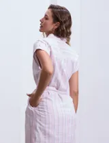 Vestido camisero corto con estampado de rayas verticales celestes y blancas. Tiene cuello camisero, mangas cortas con dobladillo, cierre frontal con botones y cinturón de lazo en la cintura.