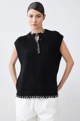 Chaleco negro de tejido de punto con cuello alto, cierre parcial con botones y detalle de pespunte blanco en el ruedo y el cuello. Sin mangas.