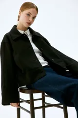 Campera corta negra de tejido de fieltro suave con cuello clásico y cierre frontal con botones. Modelo de corte holgado con hombros caídos y bolsillos insertados adelante.
