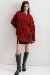 Sweater tejido de punto color fucsia con diseño de trenzas verticales en color naranja. Tiene cuello redondo y dos bolsillos frontales.