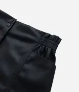 Bermuda de cuero sintético color negro, con cintura elástica, bolsillos laterales y cierre frontal con cremallera y botón.