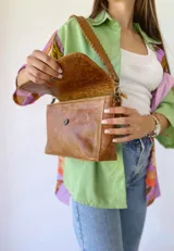 Bandolera color camel de cuero con forro de tela, correa corta con tientos y bolsillo interno.