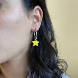 Aros de acero quirúrgico con dije en forma de estrella color amarillo, disponibles en plateado o dorado.