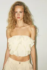 Top bandeau color crema con escote recto, hombros descubiertos y detalle de volantes en capas.