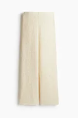 Pantalón de corte holgado color crema, confeccionado en tejido de punto con textura. Modelo de tiro alto con cintura elástica y piernas rectas.