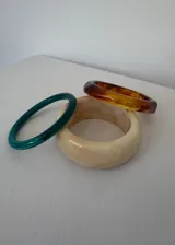 Set de tres pulseras rígidas de diferentes colores y materiales: una verde lisa, una beige con efecto marmolado y una color ámbar facetada.