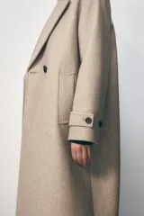 Abrigo largo color beige de cuello solapa y manga larga con trabilla y botón. Tiene bolsillos de vivo en el delantero y cierre frontal cruzado con botones.