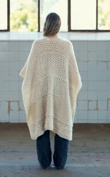 Ruana abierta color crudo, tejida a mano en crochet con lana merino uruguaya. Presenta textura combinada de puntos y trenzas, y bolsillos de cuero vacuno aplicados manualmente.
