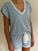 Conjunto de pijama de dos piezas color negro, compuesto por una remera de manga corta con escote en V adornado con puntilla beige, y un short con lazo frontal beige y terminación de puntilla beige en el ruedo.