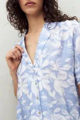 Camisa de manga corta con estampado de hojas blancas sobre fondo celeste, cuello solapa y botones de nácar al frente. Confeccionada en tejido liviano de sutil textura.