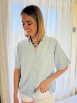 Camisa celeste de lino con mangas cortas, botones de lino y detalle drapeado en la espalda.