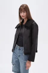 Campera negra de estilo aviador, confeccionada en material tipo gamuza o suede, con cuello y forro de corderito (shearling) negro. Presenta cierre frontal metálico y puños y ruedo con terminación de corderito.