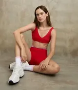 Top deportivo de microfibra color rojo, sin copa, con breteles rectos, escote en V y detalle de torcido en el busto.