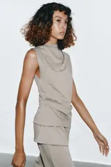 Top de algodón color beige, con cuello recto, mangas asimétricas y detalle de tejido drapeado en el lateral.