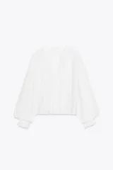 Blusa blanca de cuello solapa y manga larga abullonada terminada en volantes. Presenta bordados florales calados en el frente y cierre frontal con botones.