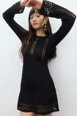 Vestido mini negro de manga larga en tejido de punto suave con escote redondo y falda con leve vuelo. Presenta secciones caladas en mangas, delantero y espalda, y secciones en punto pointelle en puños y bajo.
