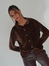 Camisa marrón de terciopelo con cuello clásico, cierre frontal con botones, mangas largas y dos bolsillos de parche en el pecho.