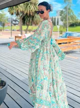 Vestido largo de polysilk con estampado paisley en tonos azul, celeste y dorado. Tiene escote en V, mangas largas acampanadas y corte amplio.